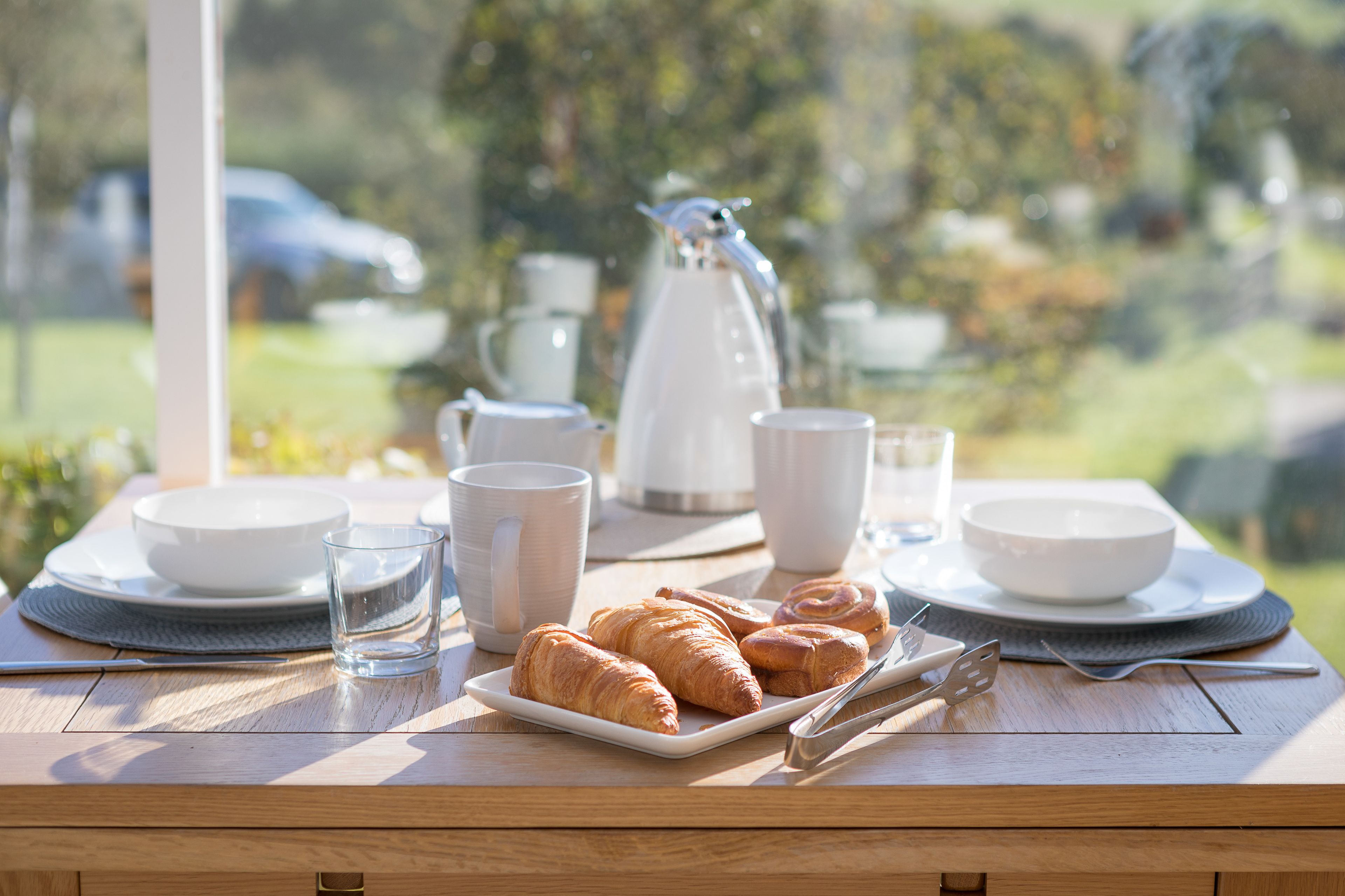 A breakfast table with croissants, coffee cups, and a teapot.