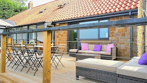 An outdoor patio area with wicker furniture, a stone wall, and a tiled roof. - My Way Guest House (Durham)