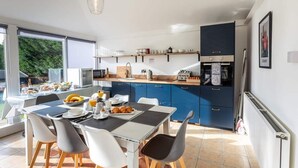 A modern kitchen with blue cabinets, a dining table with chairs, and a view of the outdoors through large windows. - My Way Guest House (Durham)