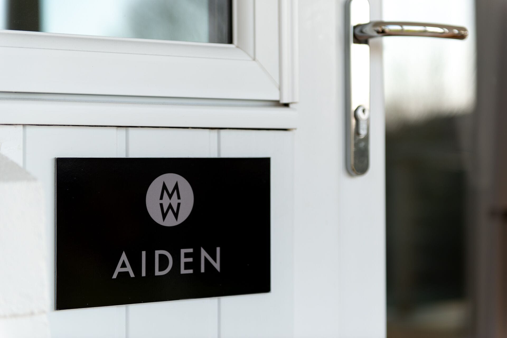Une porte avec une plaque portant le nom « AIDEN » et un logo avec les lettres « MW ».