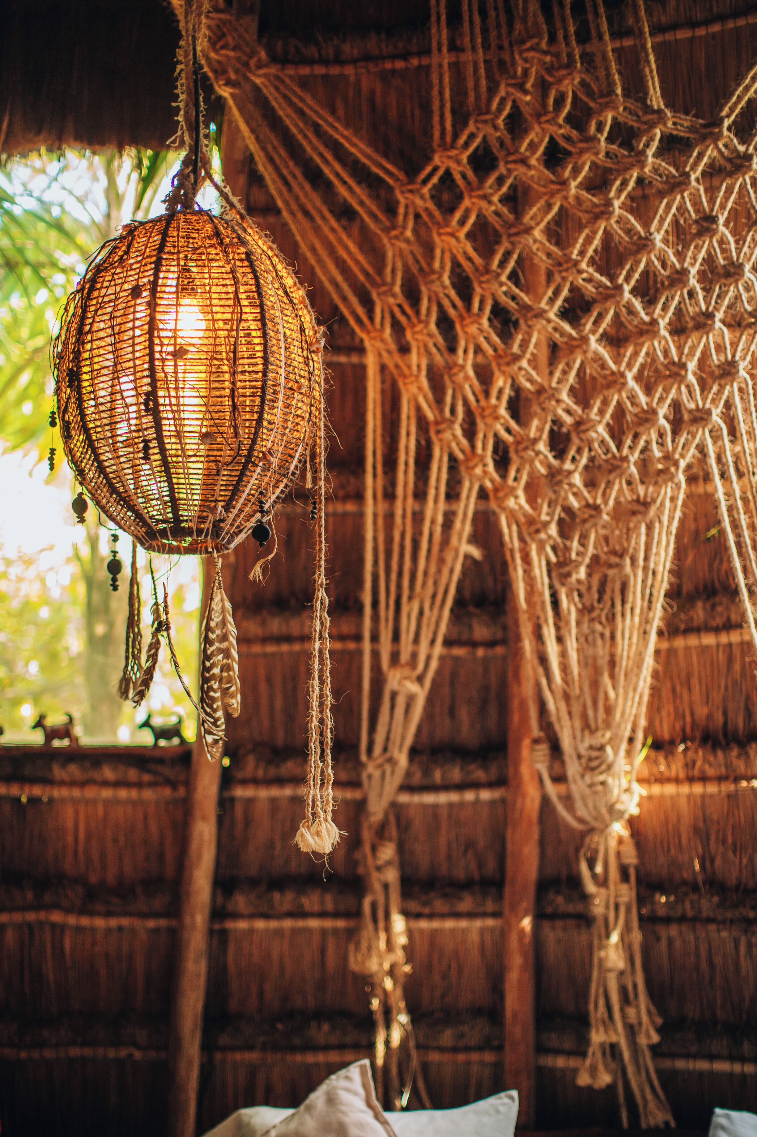 A hammock with a woven net structure hanging from a wooden ceiling, surrounded by natural light.