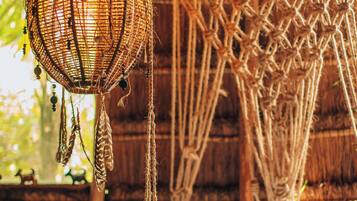 A hammock with a woven net structure hanging from a wooden ceiling, surrounded by natural light.