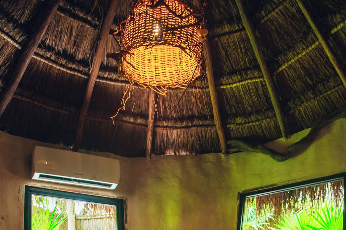 A bedroom with a bed, two windows, a ceiling fan, and a woven light fixture.