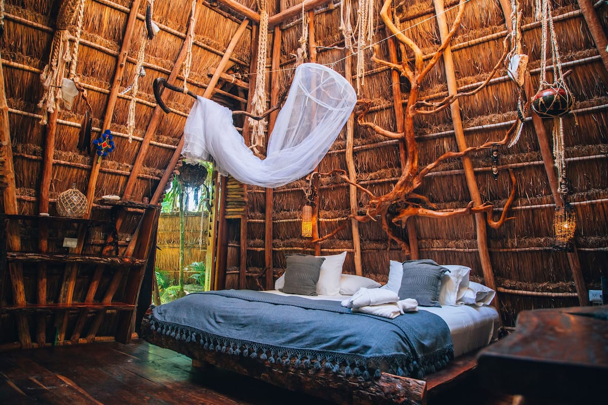 A rustic room with a bed, wooden furniture, and a thatched ceiling.
