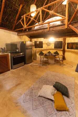 A rustic kitchen with a stove, refrigerator, and dining area with chairs and a table.
