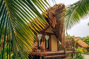 Une cabane à toit de chaume avec une véranda en bois, deux chaises en bois et un hamac.
