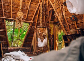 A rustic thatched-roof hut with a view of lush greenery outside.