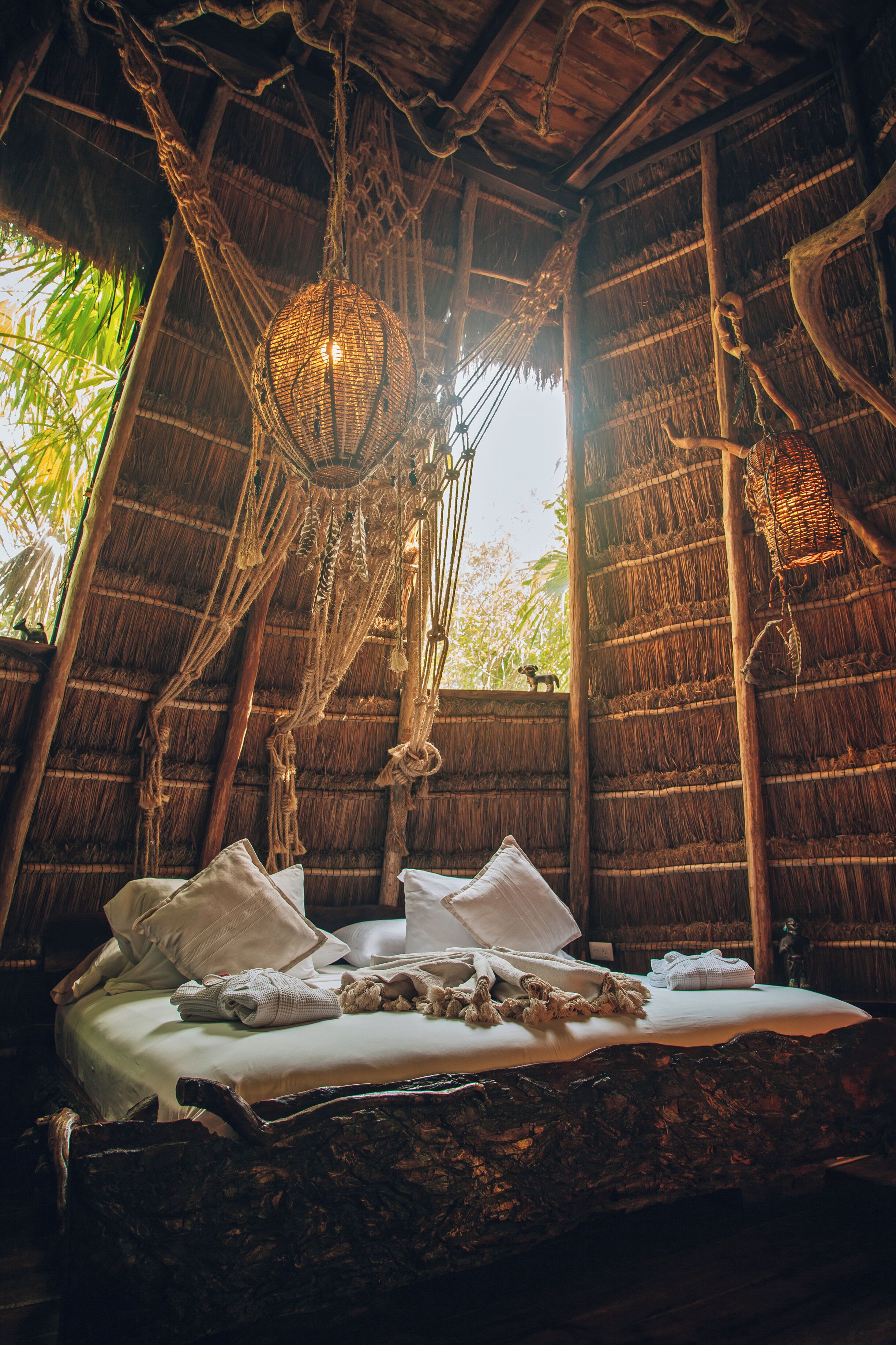 Una habitación rústica con cama, techo de paja y una lámpara colgante.