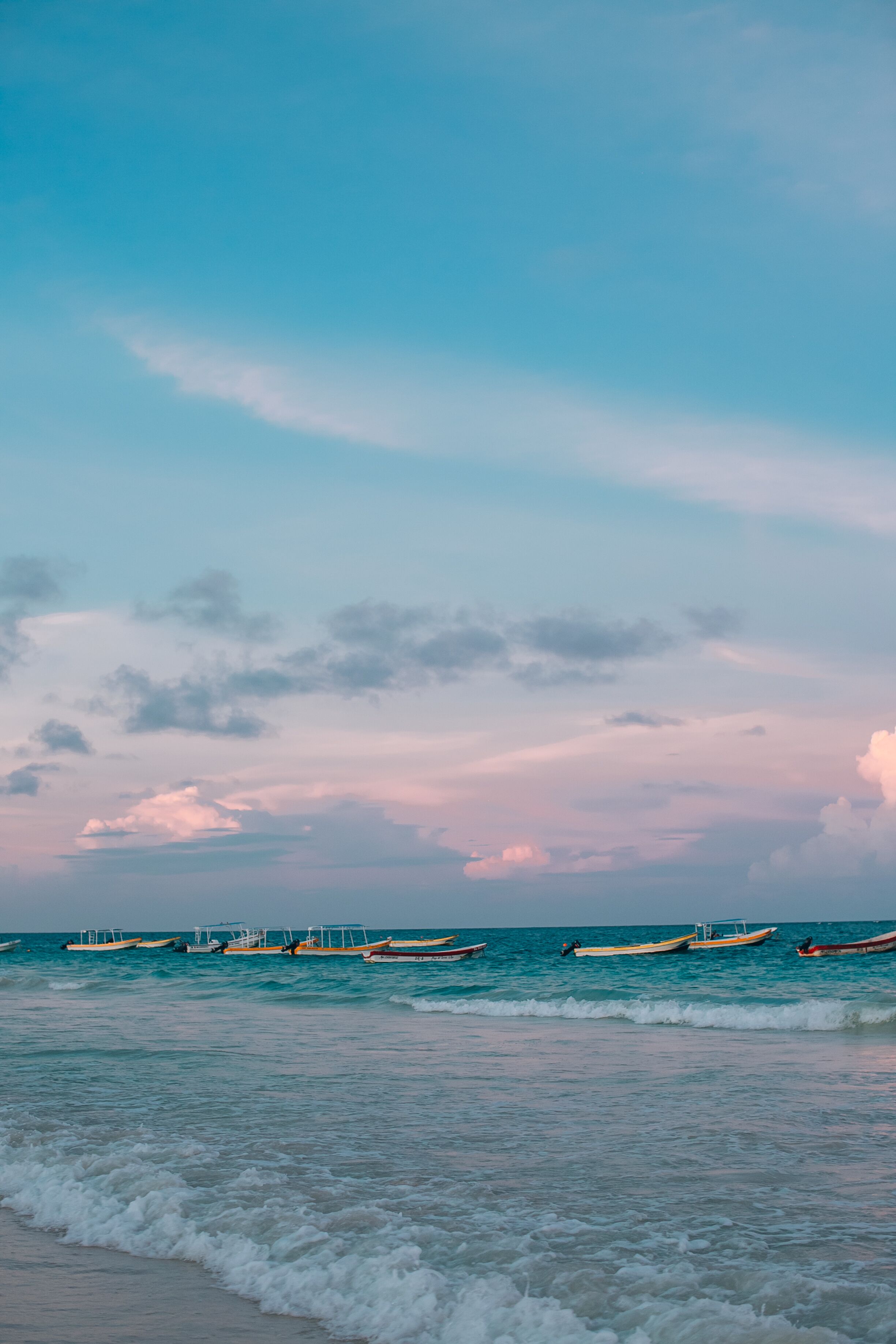 A beach with boats and a pier in the distance.