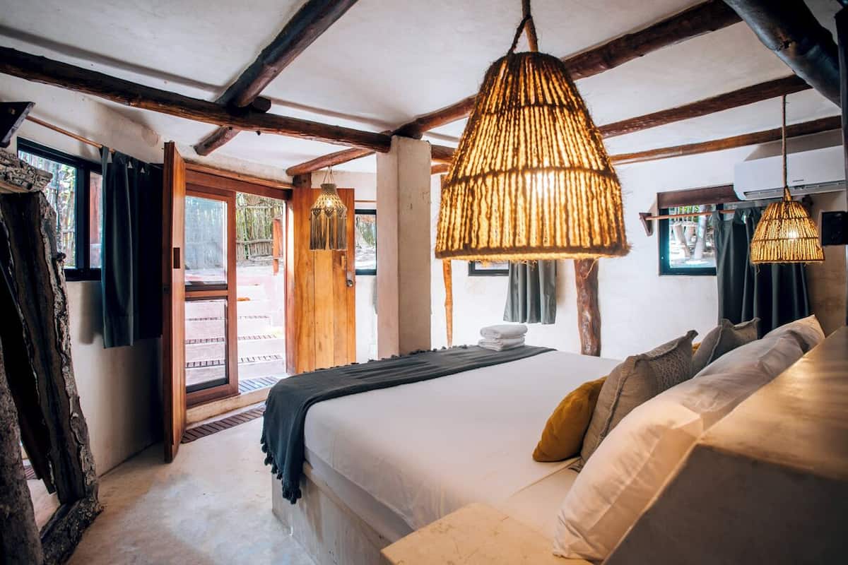 A bedroom with a large bed, wooden beams, and a hanging light fixture.