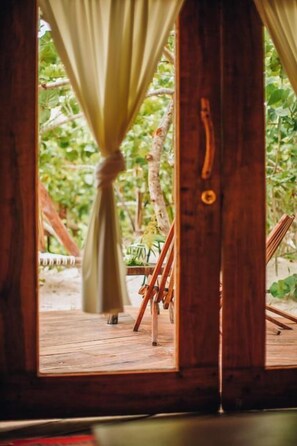 A wooden door with a curtain tied at the top, leading to an outdoor wooden deck with a chair and a table.