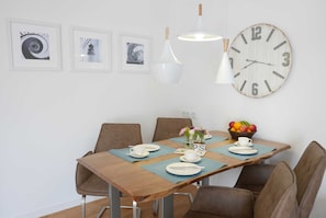 Un comedor con una mesa de madera, cuatro sillas, un reloj de pared grande y cuadros enmarcados.
