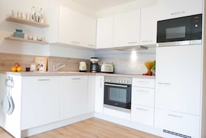 Una cocina moderna con armarios blancos, horno empotrado, microondas y cafetera.