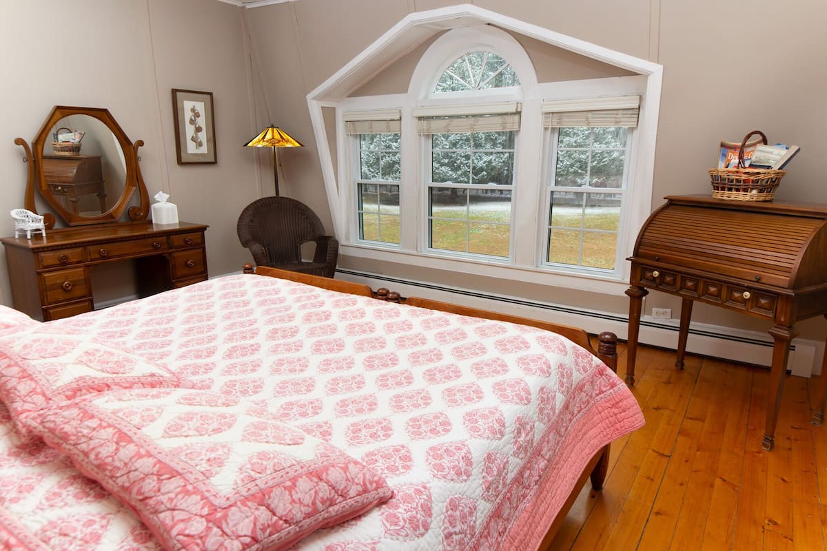 A bedroom with a large bed, a dresser, a chair, a lamp, a window, and a piano.