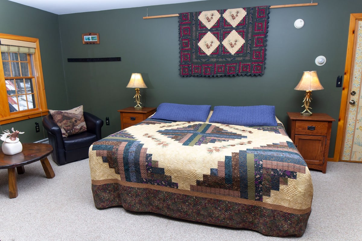 A bedroom with a large bed, two nightstands, a chair, and a window.