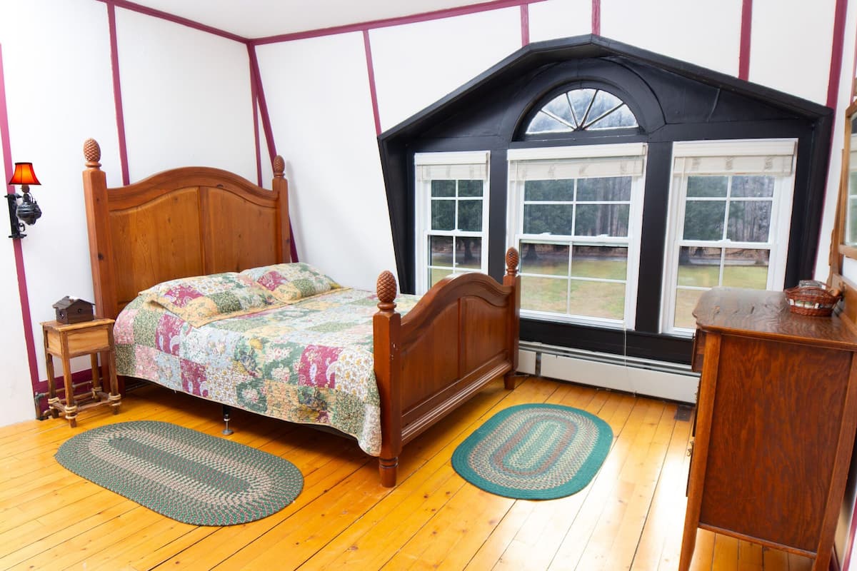 A bedroom with a wooden bed, a window with multiple panes, and a wooden dresser.
