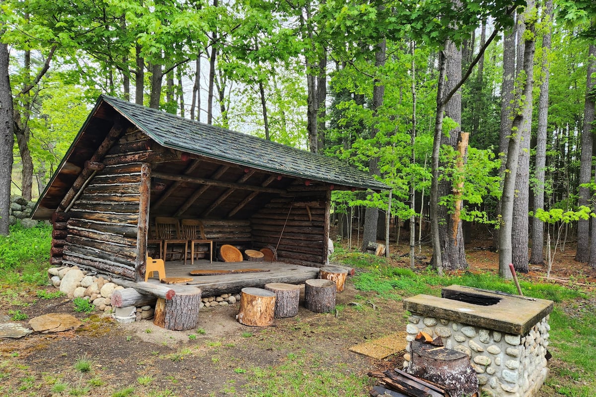 A rustic log cabin with a stone fireplace, surrounded by a forest.