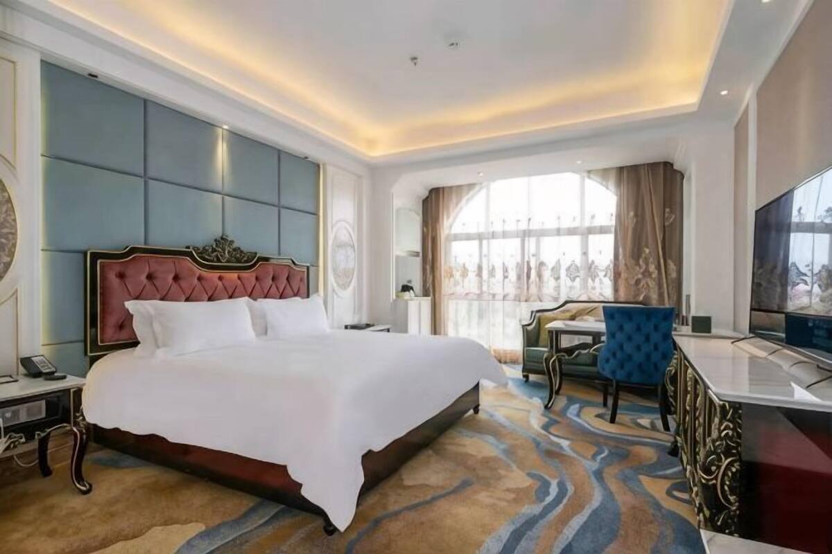 A hotel room with a large bed, a TV, a desk, and a view of the outdoors.