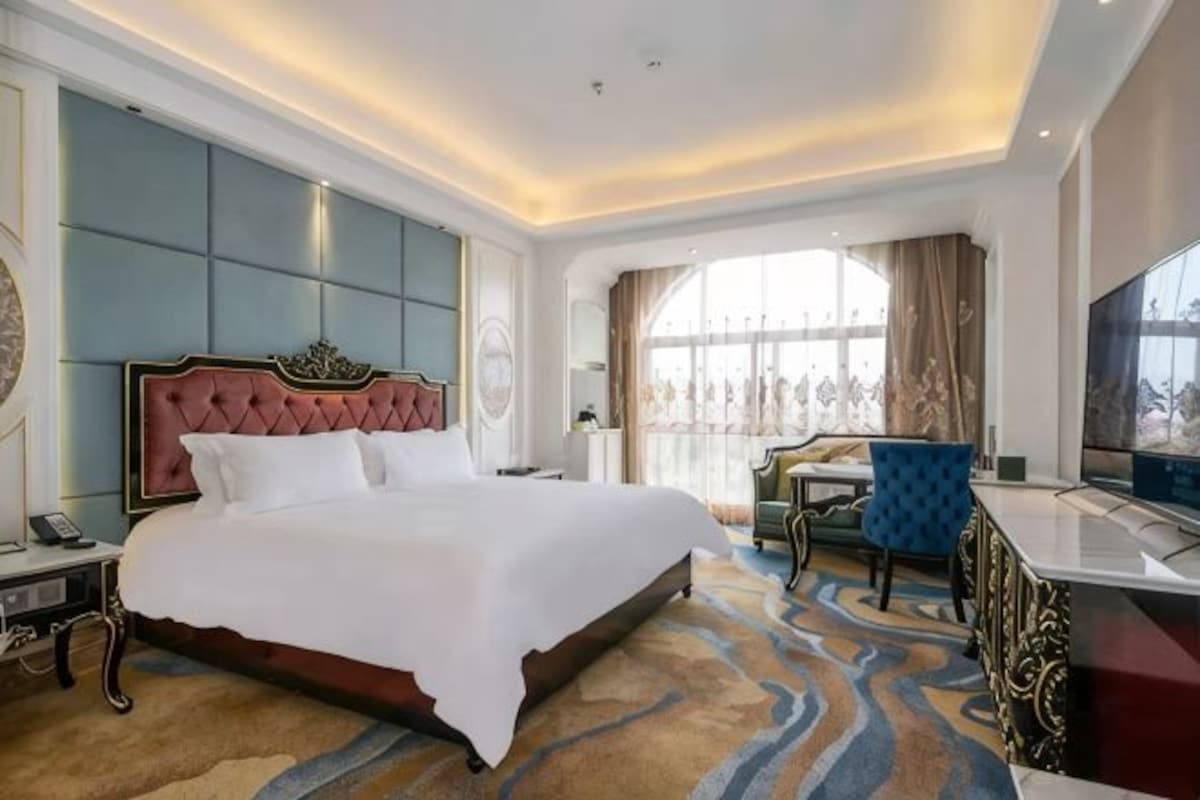A hotel room with a large bed, a TV, a desk, and a view of the outdoors.