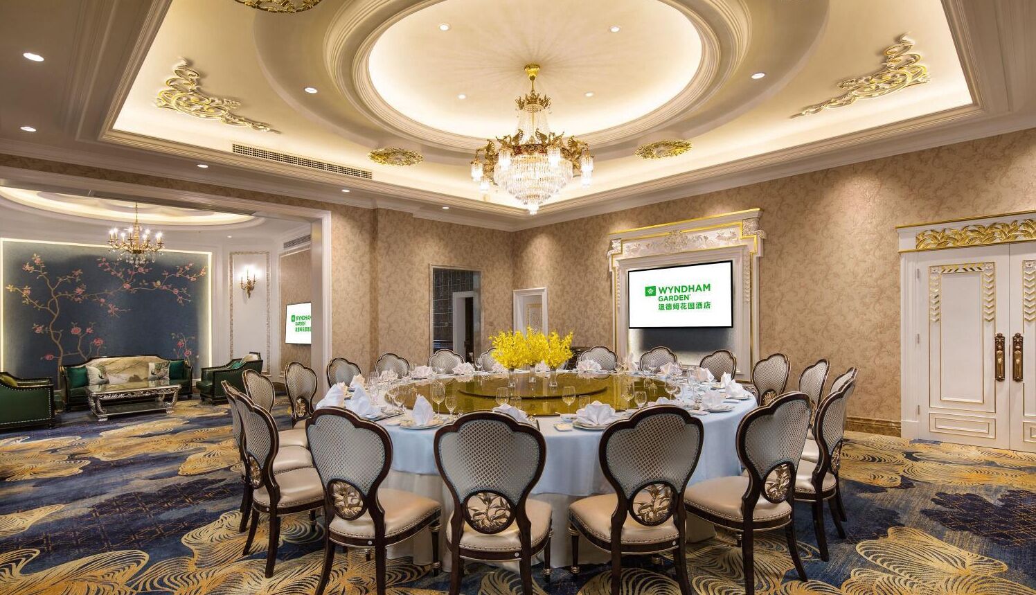 Un salón de banquetes con una mesa redonda dispuesta para un evento formal, rodeado de sillas tapizadas.