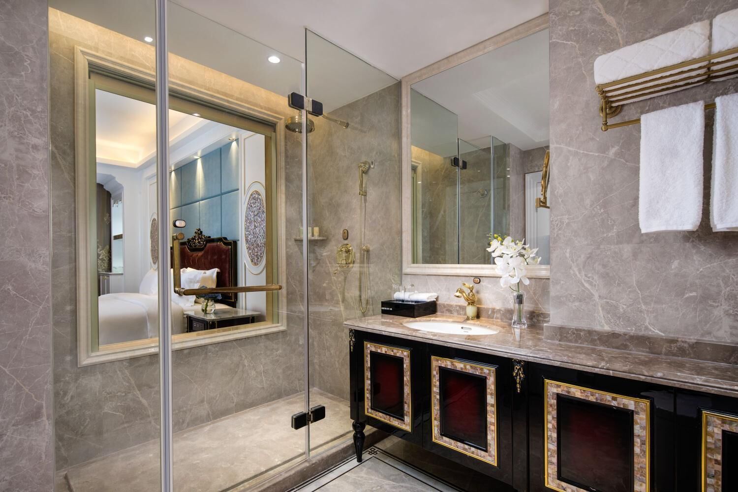 A modern bathroom with a glass-enclosed shower, a vanity with gold trim, and a large mirror reflecting the room.