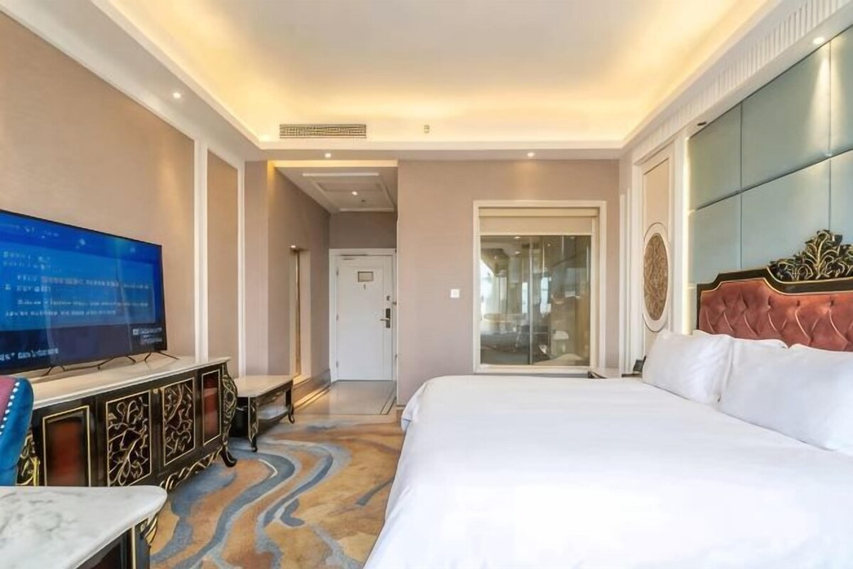 A hotel room with a large bed, a television, a desk, and a bathroom visible through an open door.