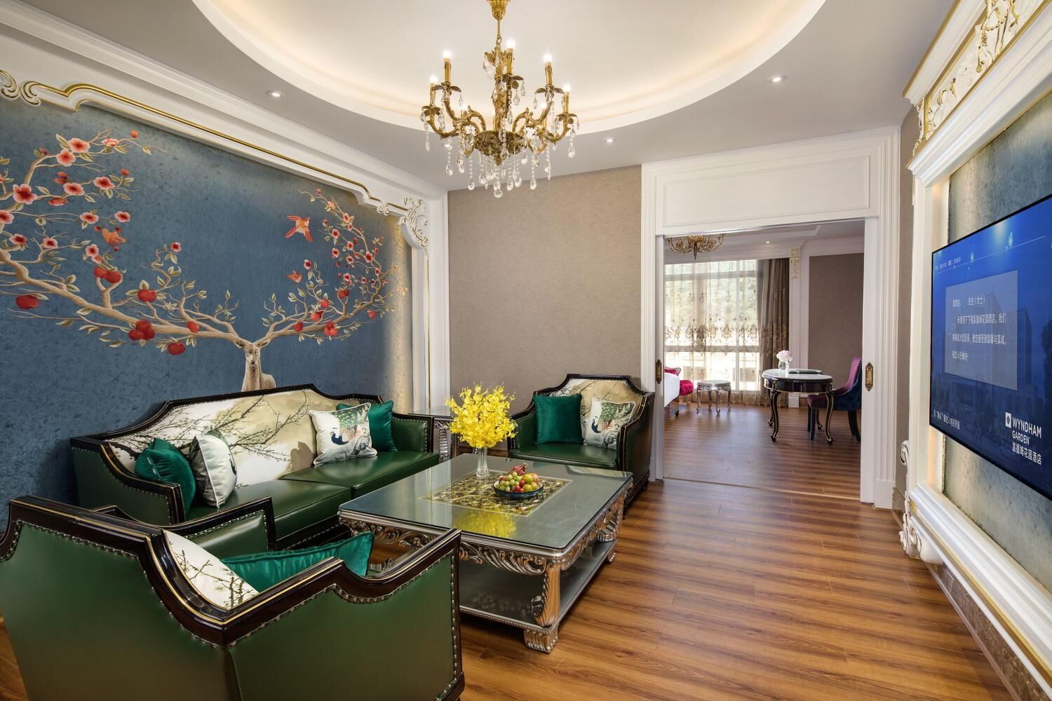 A luxurious living room with a green sofa set, a chandelier, and a wall mural.