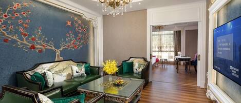 A luxurious living room with a green sofa set, a chandelier, and a wall mural.