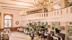 A spacious hotel lobby with multiple dining tables, comfortable seating, a large floral arrangement, and a chandelier. - Grand Hotel Sole (Nitra)