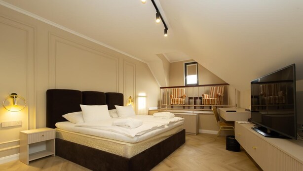 A bedroom with a large bed, a desk, a TV, and a staircase. - Grand Hotel Sole (Nitra)