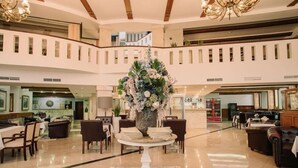 A spacious lobby with a central floral arrangement, multiple seating areas, and a high ceiling with wooden beams. - Grand Hotel Sole (Nitra)