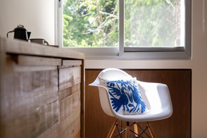 Une chambre moderne avec un mur en bois, une chaise blanche avec un coussin bleu et une fenêtre donnant sur des arbres.