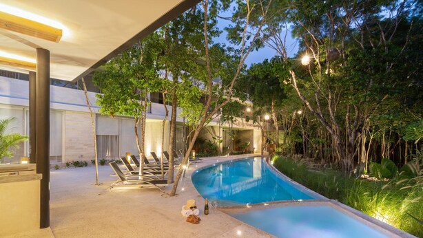 Ein Pool mit Liegestühlen, umgeben von Bäumen und einem modernen Gebäude.