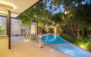 Une piscine entourée d’arbres et bordée de chaises longues, avec un bâtiment moderne en arrière-plan.