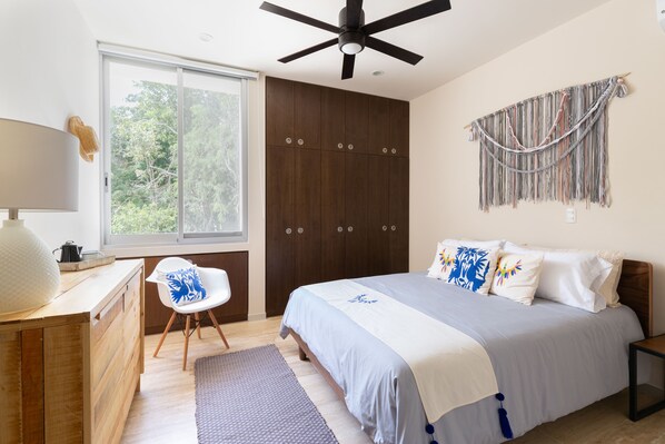 Une chambre à coucher comprenant un lit, un bureau, une chaise, un ventilateur de plafond, une fenêtre et un tableau ou une décoration murale.