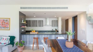 A modern kitchen with a central island, wooden stools, a dining table with a patterned runner, and a potted plant. - Casa Julian 2BR - Attha Cenote (Tulum)