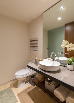 A modern bathroom with a white toilet, a round sink, a mirror, and a wooden cabinet. - Casa Luna 1BR by the Pool - Attha Cenote (Tulum)