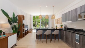 A modern kitchen with a central island, bar stools, pendant lighting, and a view of greenery outside. - Casa Luna 1BR by the Pool - Attha Cenote (Tulum)