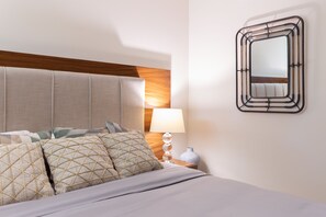 A neatly made bed with patterned pillows, a bedside lamp, and a wall-mounted mirror.