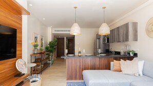 A modern living room with a sofa, a TV, and a kitchen area with a bar. - Casa Sol 1BR by the Pool - Attha Cenote (Tulum)