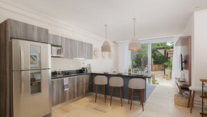A modern kitchen with a built-in refrigerator, a microwave, and a dining area with bar stools. - Casa Sol 1BR by the Pool - Attha Cenote (Tulum)
