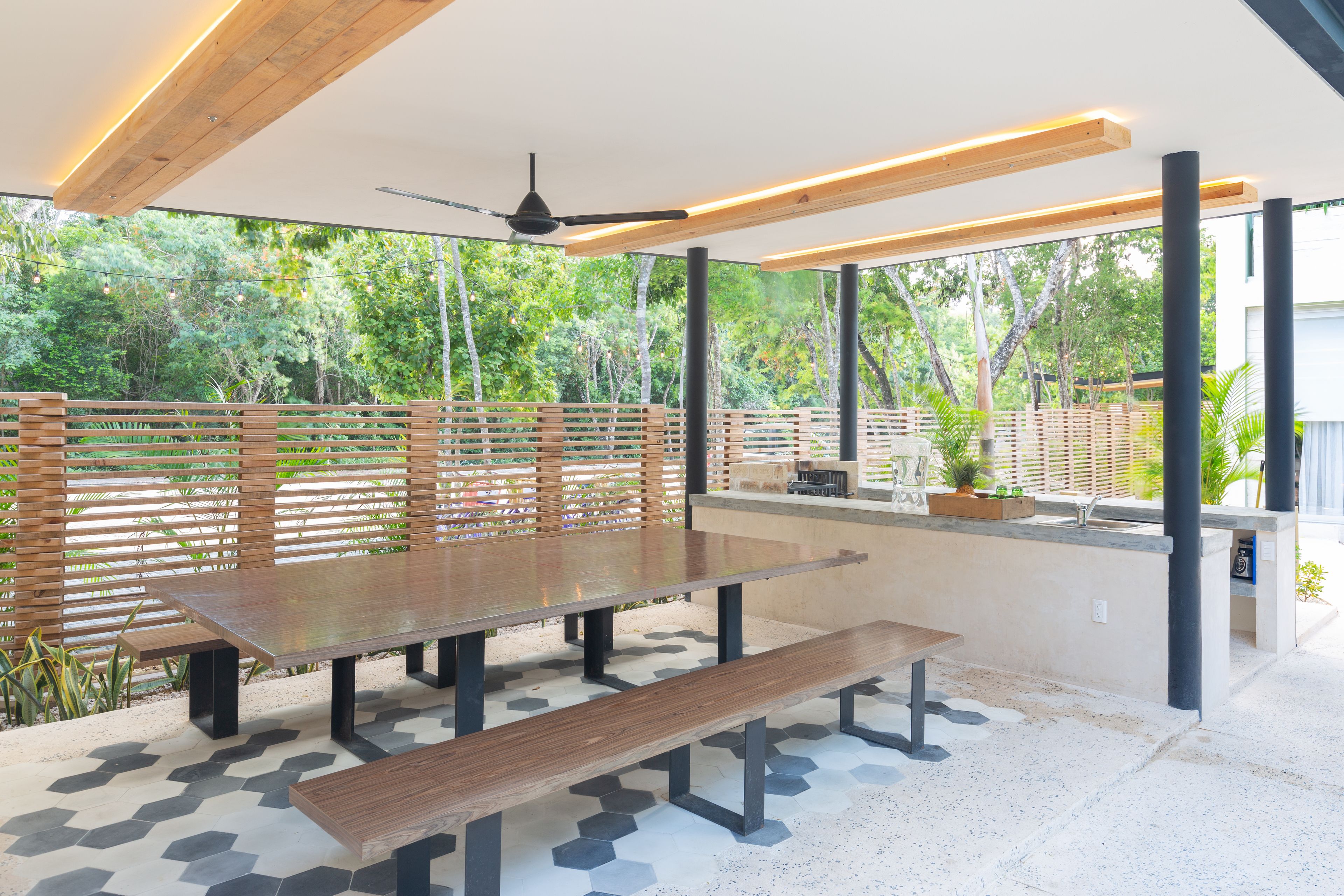 An outdoor patio with a wooden table and benches, surrounded by a wooden fence and potted plants.