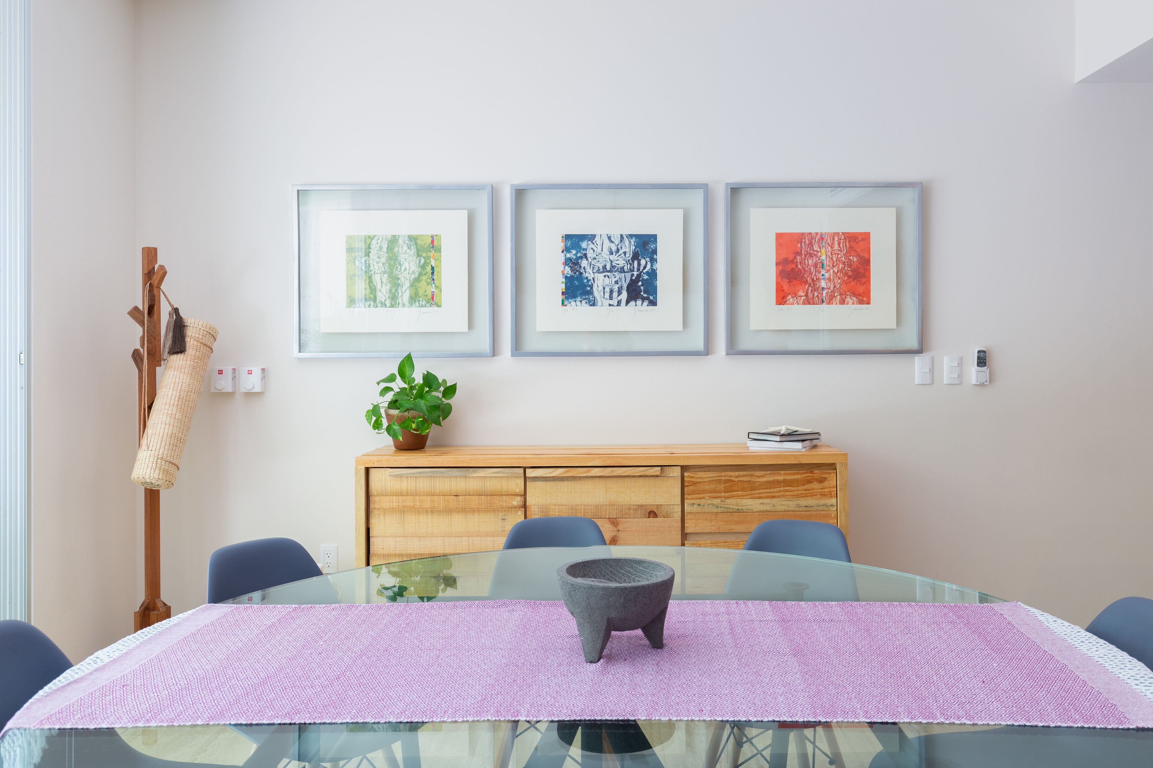 Un espace repas moderne avec une table en verre, un chemin de table violet et des œuvres d’art encadrées accrochées au mur.