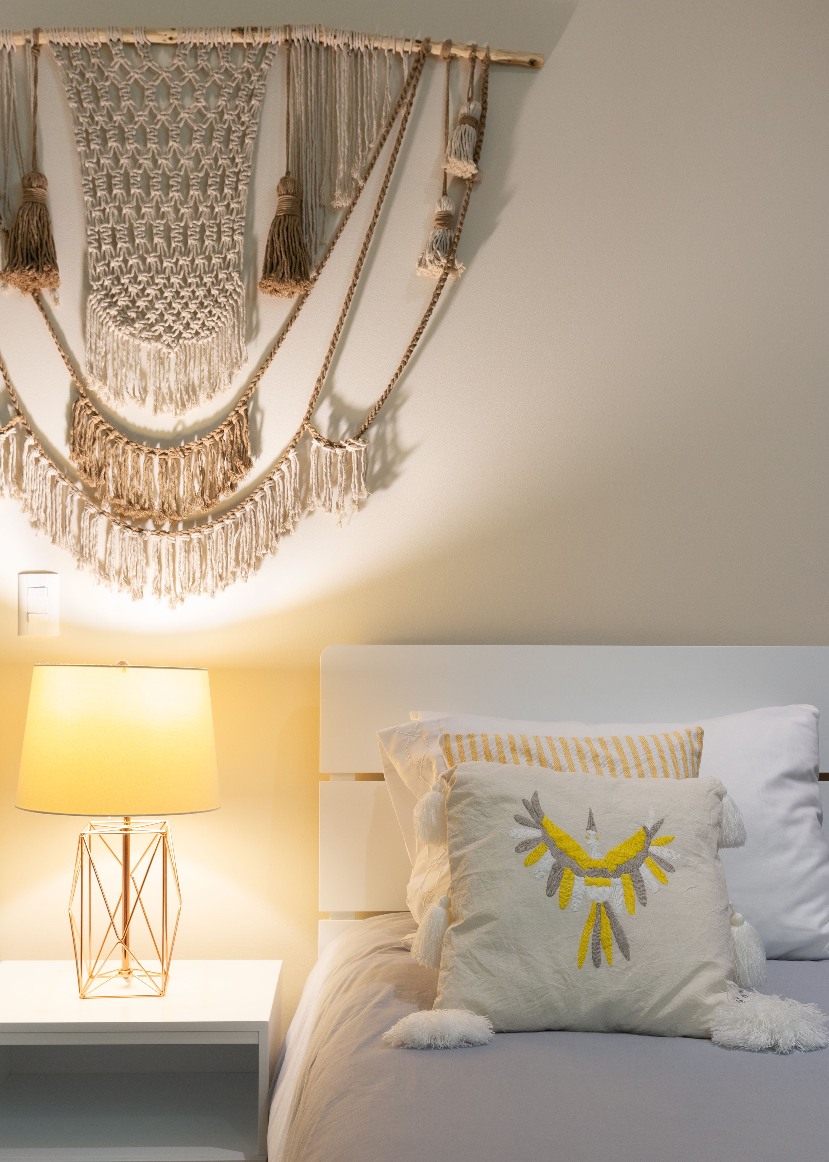 Une chambre à coucher avec une décoration murale en macramé, une lampe de chevet et des coussins décoratifs.