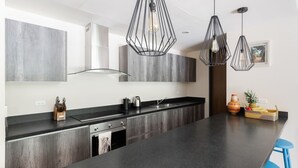 Una cocina moderna con una isla grande, encimeras oscuras y lámparas colgantes.