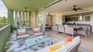 A spacious balcony with a dining area, seating, and a kitchen visible through the glass doors. - Villa Parota 2BR Nature Views - Attha Cenote (Tulum)