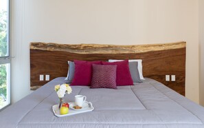 Una cama bien tendida con un cabecero de madera, una bandeja con una taza, una manzana y flores.