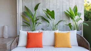 A bed with white and orange pillows, a wicker headboard, and large green plants in pots against a concrete wall. - Villa Parota 2BR Nature Views - Attha Cenote (Tulum)