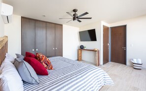 A bedroom with a bed, a ceiling fan, a TV, and a wardrobe.