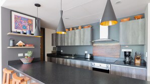 A modern kitchen with a black countertop, stainless steel appliances, and wooden bar stools. - Casa Marisol 2BR Tulum Spirit - Attha Cenote (Tulum)